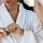 Young woman applying skincare cream in a bathrobe, reflecting self-care and wellness at home.