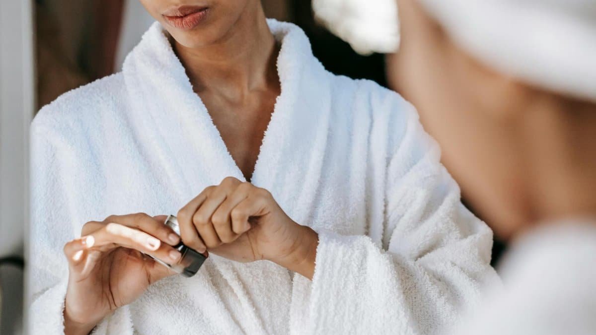 Young woman applying skincare cream in a bathrobe, reflecting self-care and wellness at home.