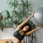 A woman stretches with a yoga ball surrounded by lush indoor plants, embracing healthy living.