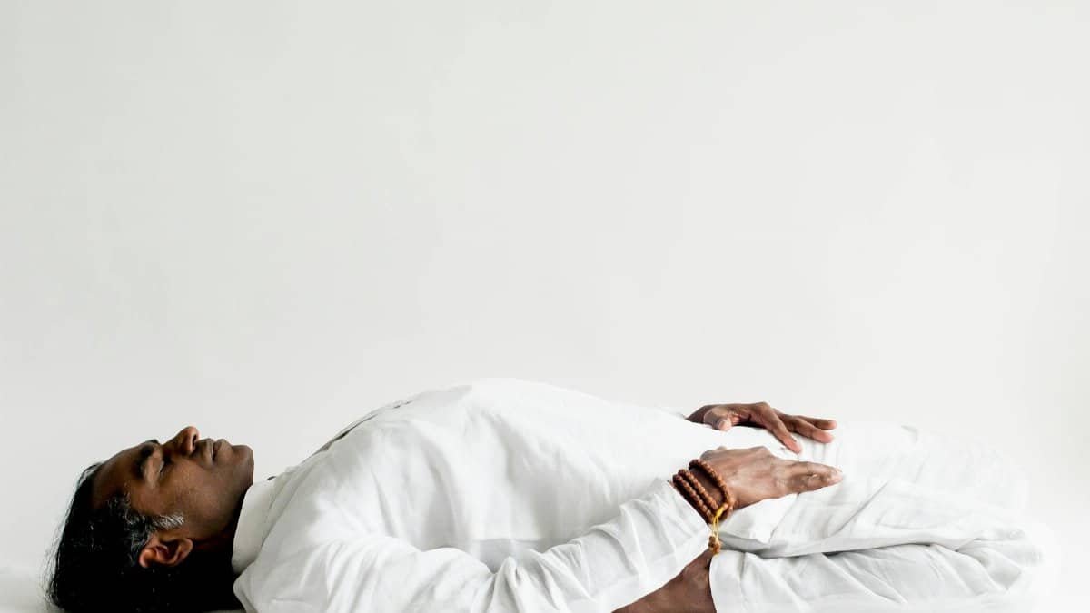 A person in a white outfit practicing meditation, lying down peacefully indoors.