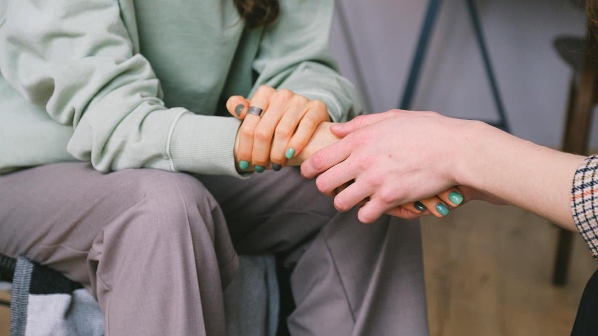 Close-up of two people holding hands during a comforting therapy session.