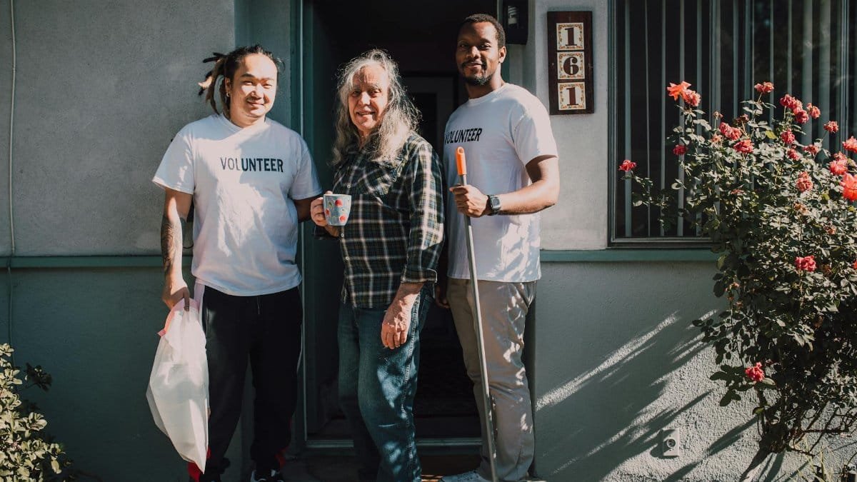 Two volunteers assist a community member outside their home, fostering social good.
