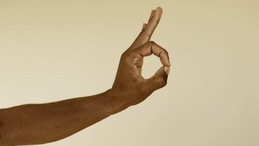 Close-up image of a hand making an OK gesture on a beige background.
