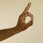 Close-up image of a hand making an OK gesture on a beige background.