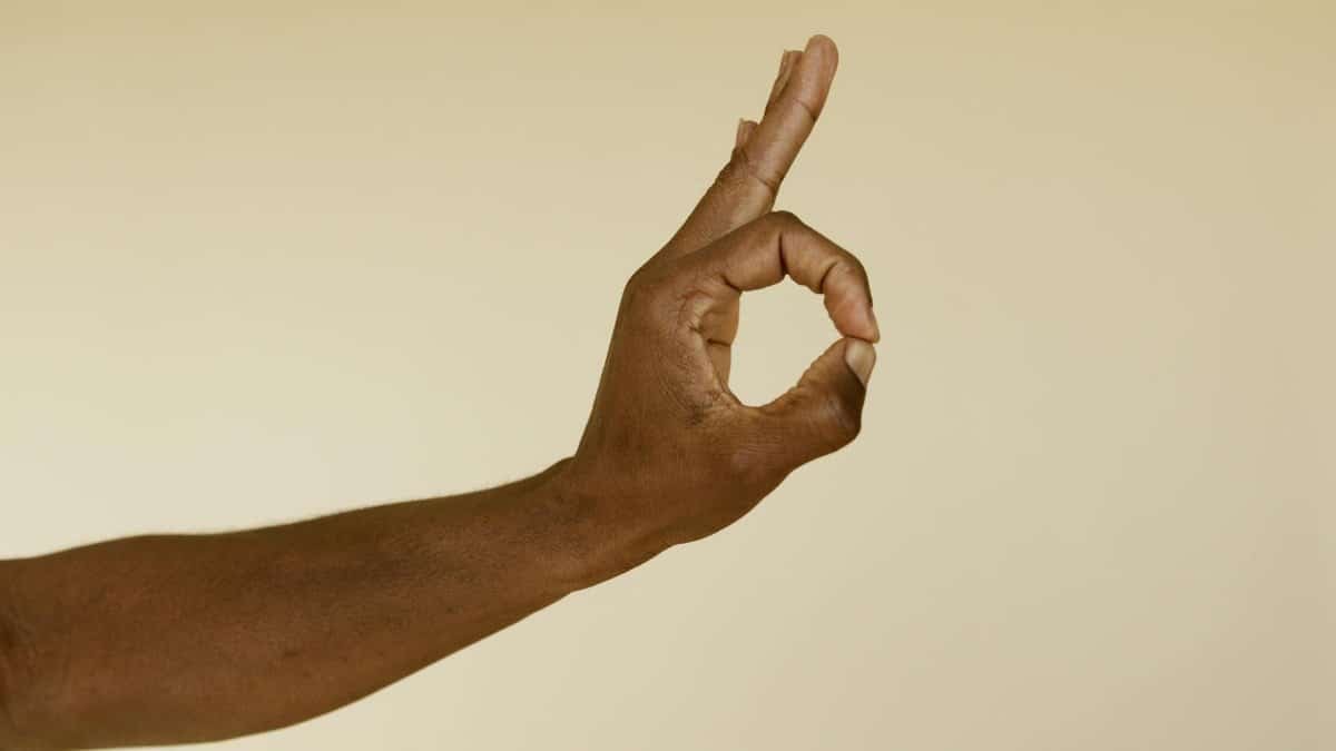 Close-up image of a hand making an OK gesture on a beige background.