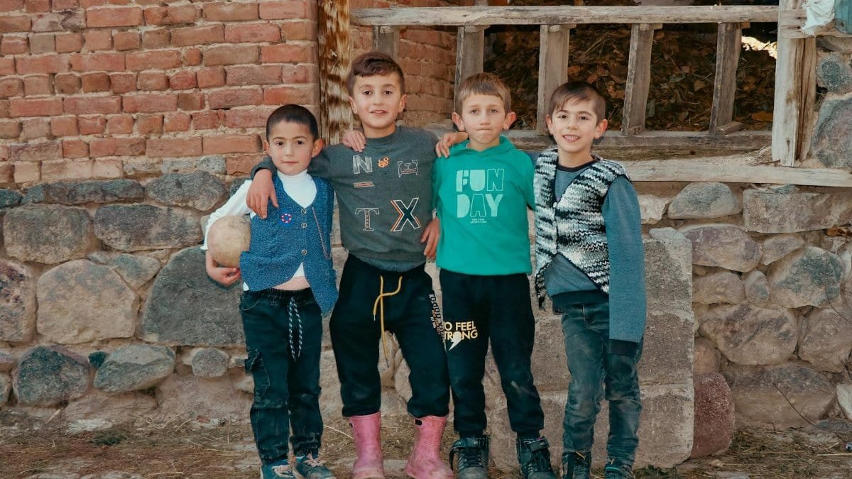 Group of boys posing cheerfully outside against a rustic brick and stone wall.