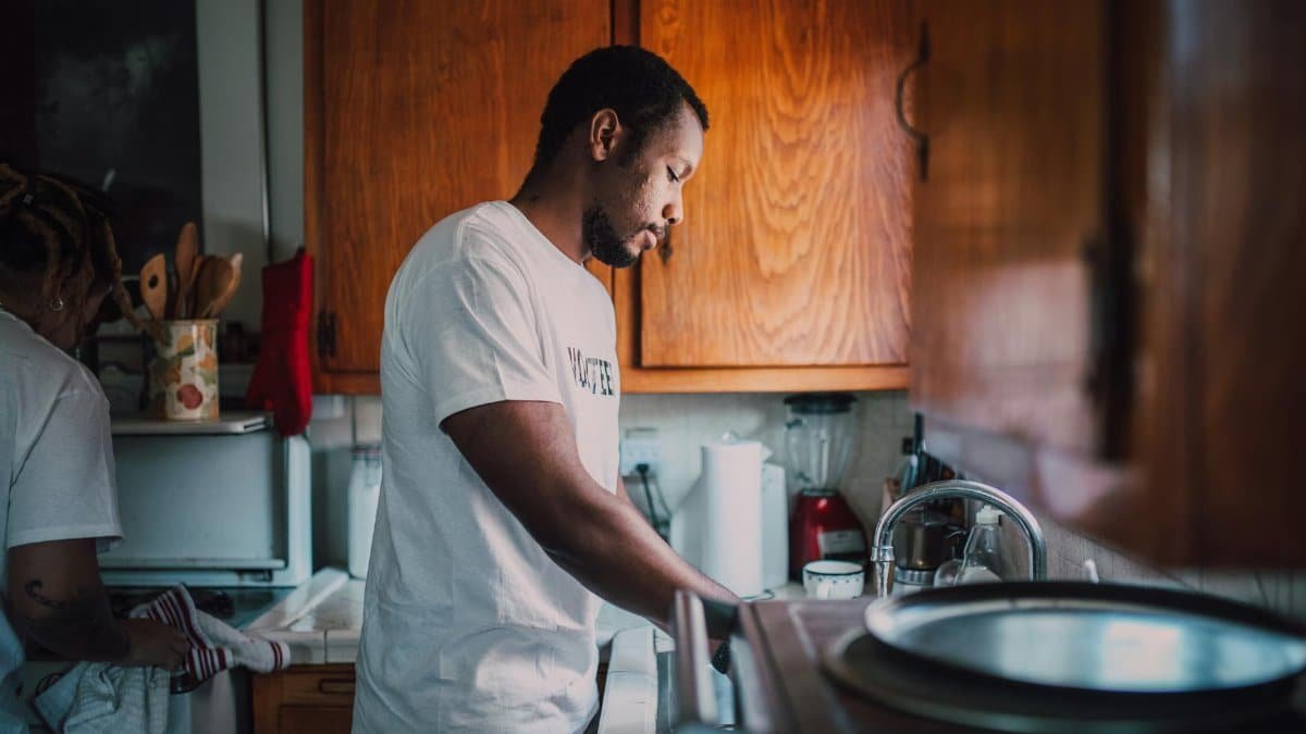 A man and woman volunteer wash dishes in a kitchen, helping their community.