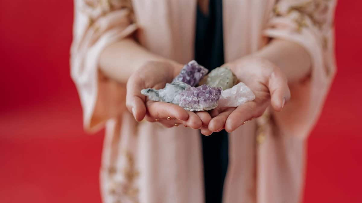 Elegant hands holding healing crystals against a vibrant red background.