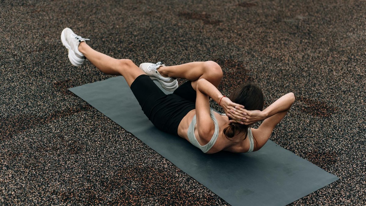 Fit woman doing a bicycle crunch on a mat outdoors, emphasizing core strength and fitness.