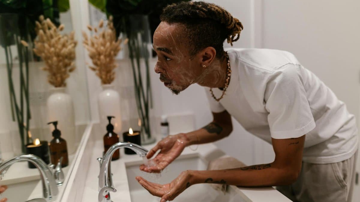 Man washing face in bathroom sink, showcasing a morning skincare routine for hygiene.