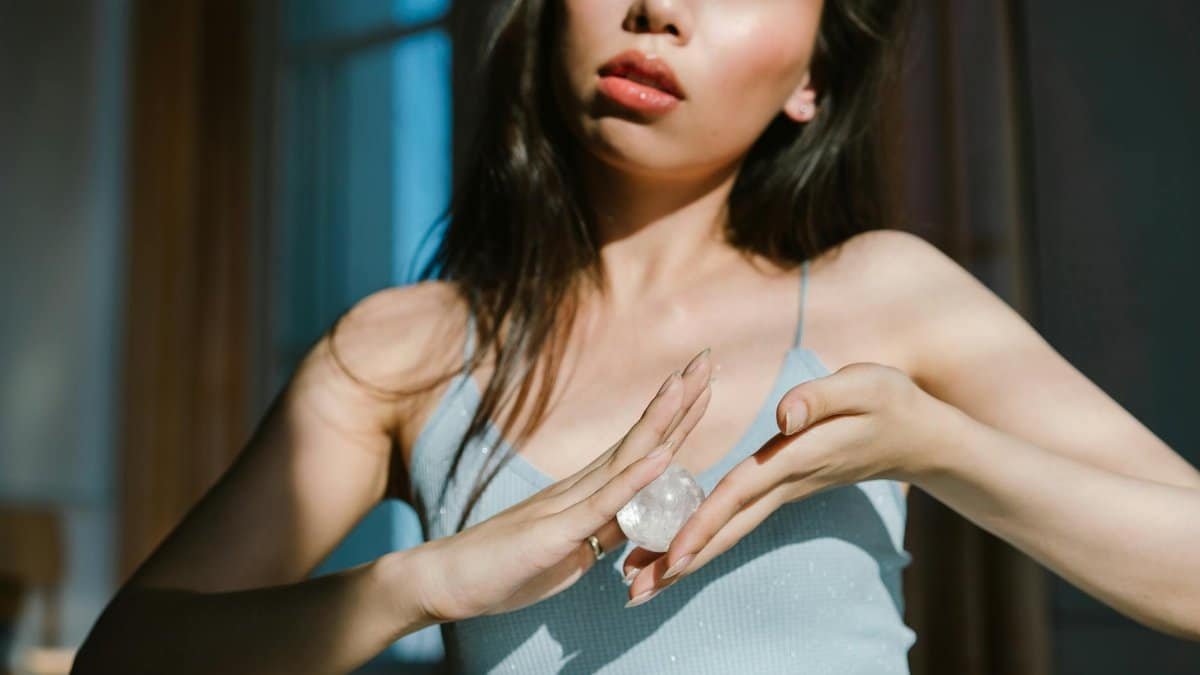 A serene woman holds a crystal indoors, basking in warm sunlight, emphasizing tranquility and spiritual energy.
