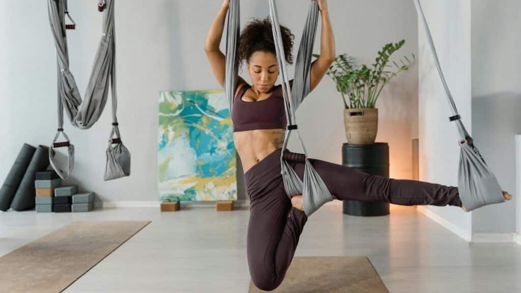 Woman performing aerial yoga indoors, showcasing strength and flexibility on hanging silks.