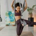 Woman performing aerial yoga indoors, showcasing strength and flexibility on hanging silks.