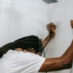 A man stands under a shower with head bowed, depicting contemplation and reflection.