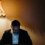 A senior man with a beard reads by a lamp in a cozy indoor setting, capturing a sense of tranquility.