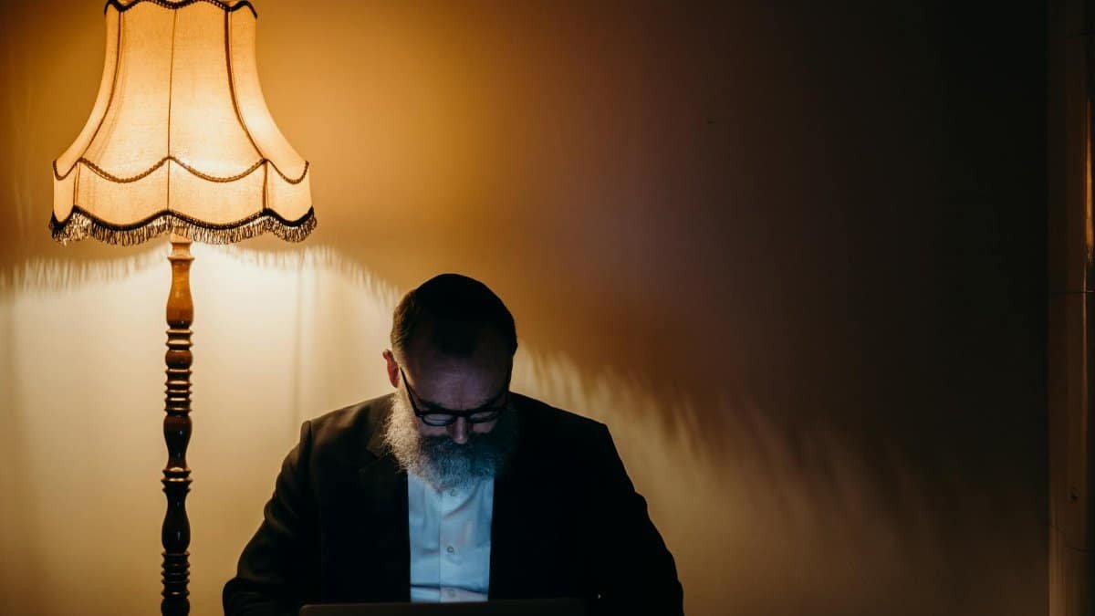 A senior man with a beard reads by a lamp in a cozy indoor setting, capturing a sense of tranquility.