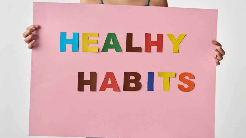 A woman holds a pink poster with colorful letters spelling 'HEALTHY HABITS'.