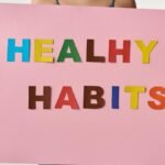 A woman holds a pink poster with colorful letters spelling 'HEALTHY HABITS'.