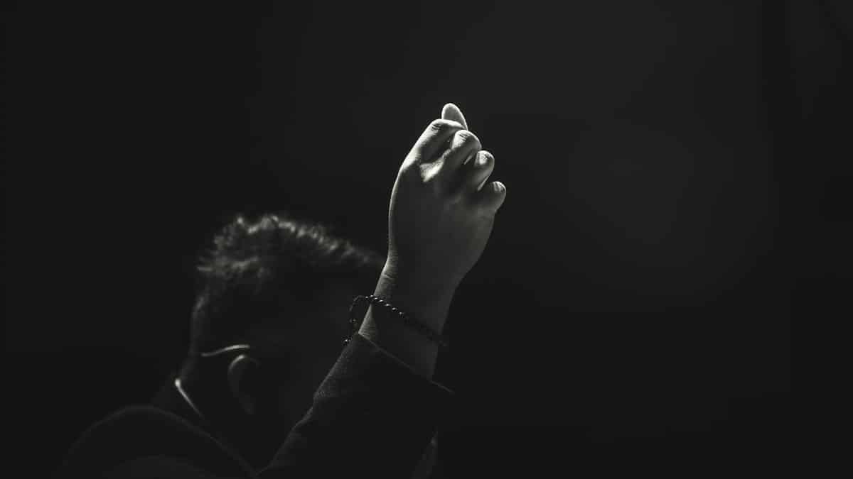 Artistic black and white image of a raised hand in focus against a dark background.