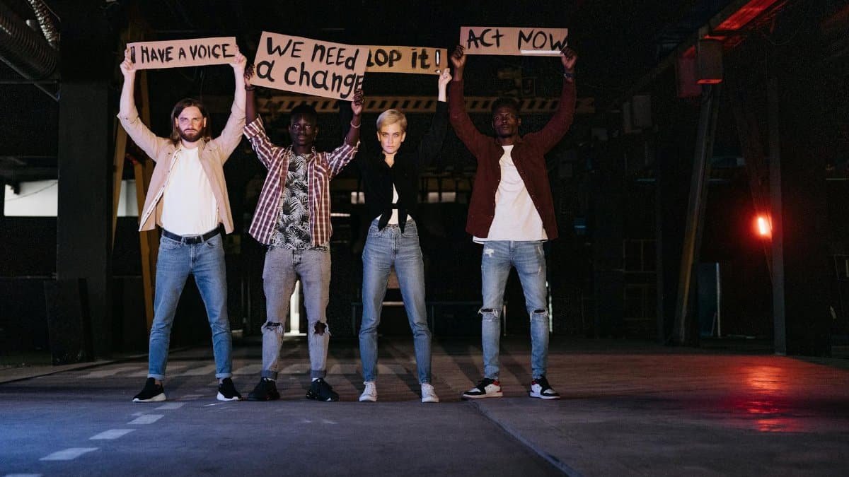 A diverse group of activists holding protest signs indoors at night, calling for change.
