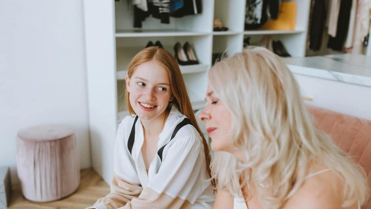 Two women smiling and bonding, seated in a modern wardrobe room, conveying positive emotions.