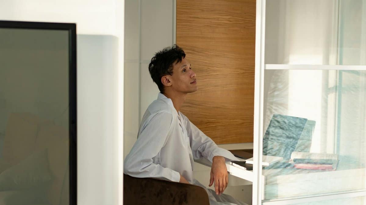 An adult man sitting in a bright, modern home office space with a thoughtful expression.