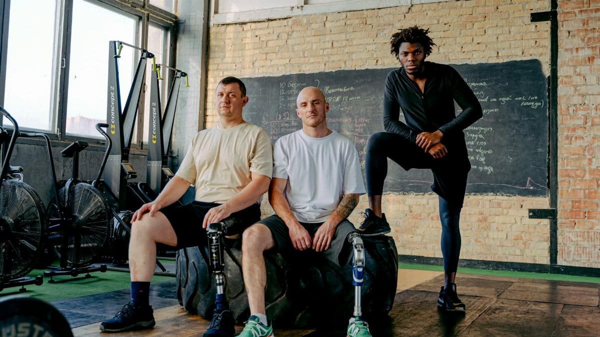 Diverse group of men with prosthetic legs posing confidently in a gym setting, showcasing strength and inclusivity.