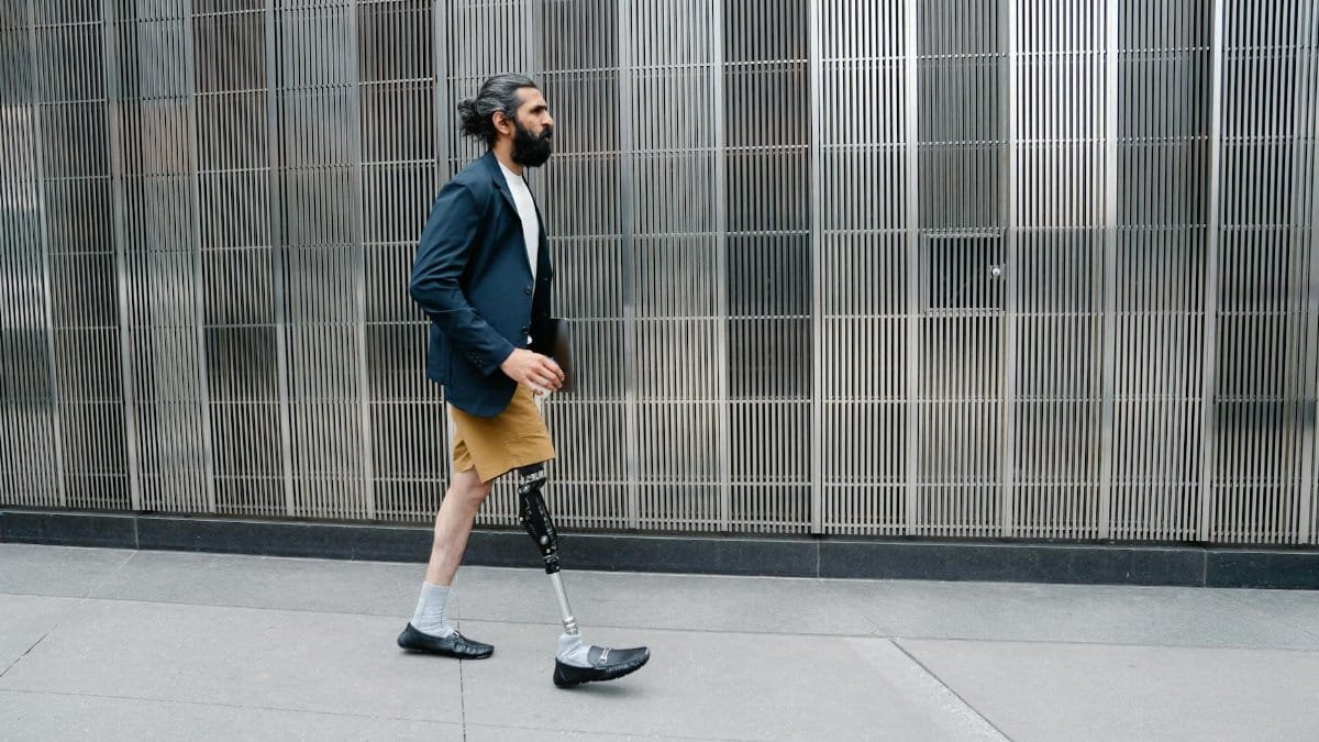Confident man with prosthetic leg walks by modern building facade, showcasing empowerment.