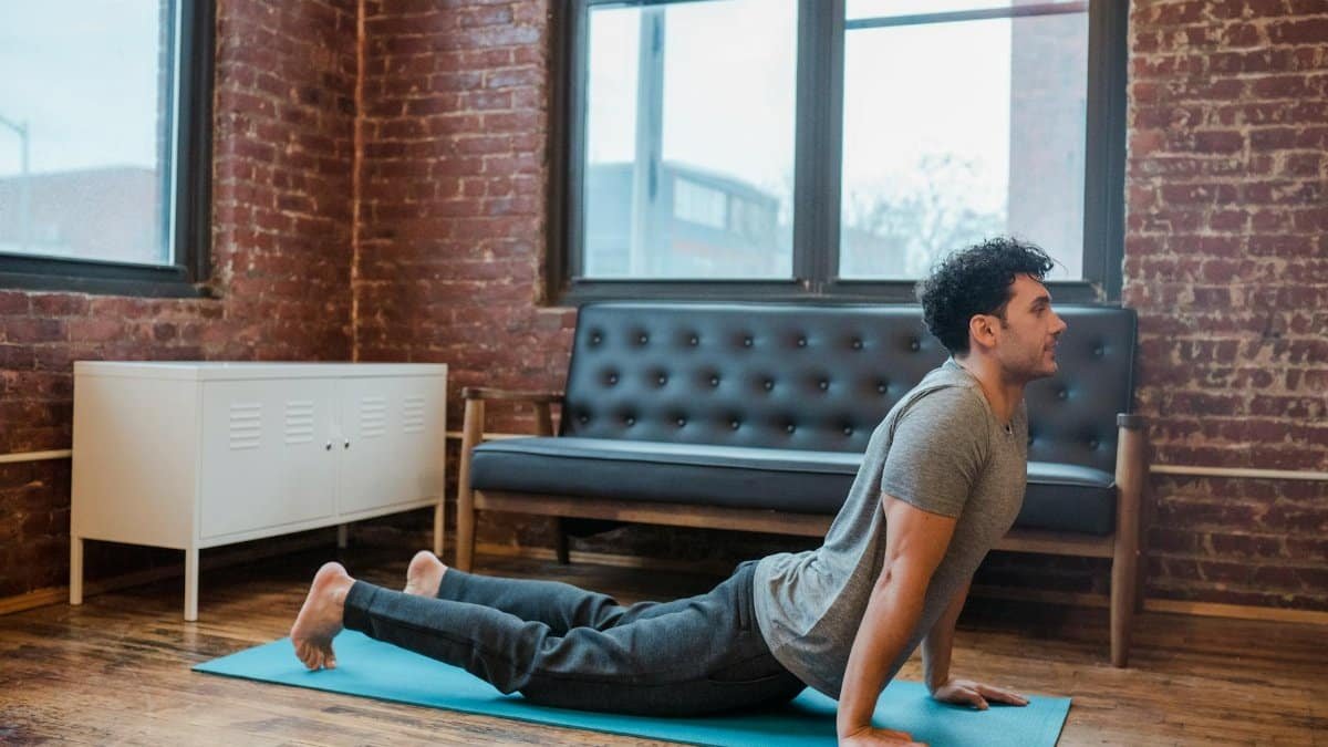 Side view full body of concentrated male lying on sports mat and stretching back muscles in Bhujangasana during yoga training