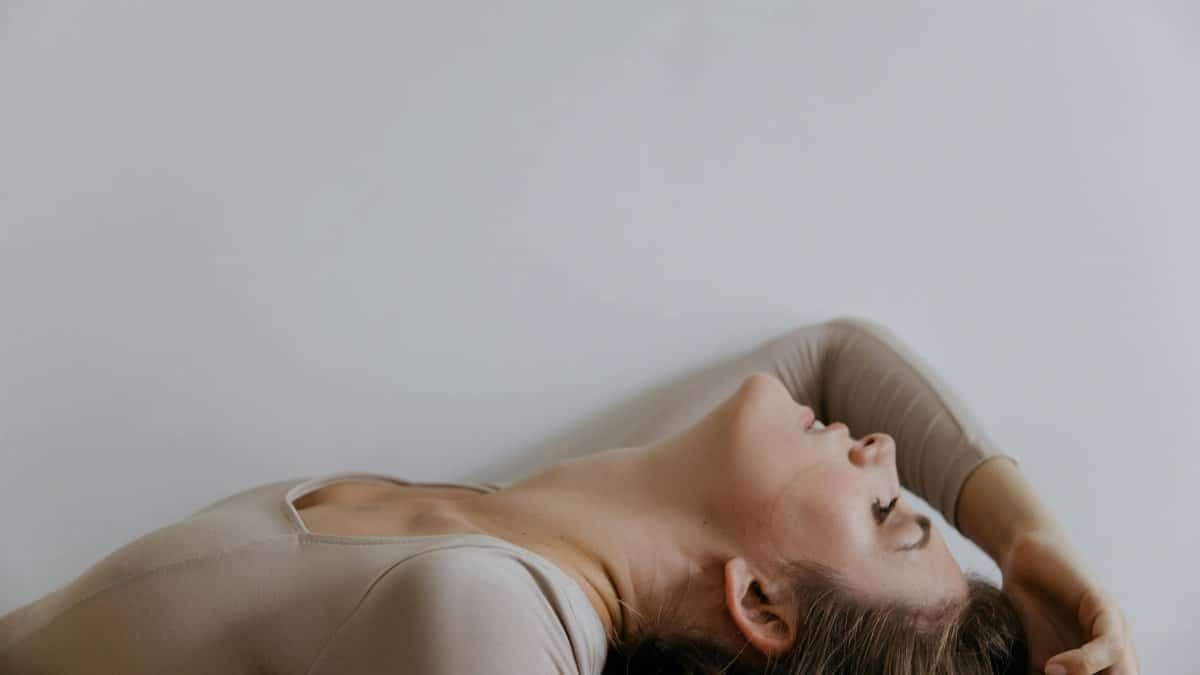 A woman in a beige top lying back against a neutral background, offering ample copy space.