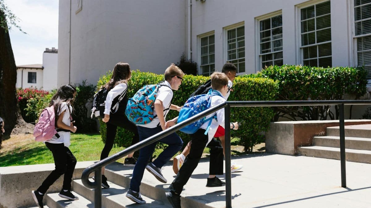 Children joyfully running up steps to school, backpacks in tow, showcasing school life.