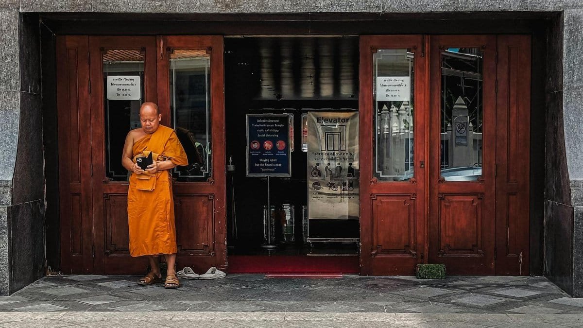 A Tibetan monk stands by a wooden entrance, captured outdoors during the day.
