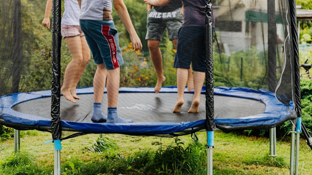 Group of kids jumping and playing on an outdoor trampoline in a backyard.