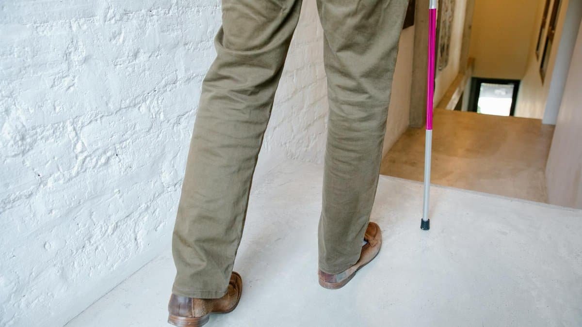 A person using a walking stick navigates a hallway, symbolizing independence and mobility support.