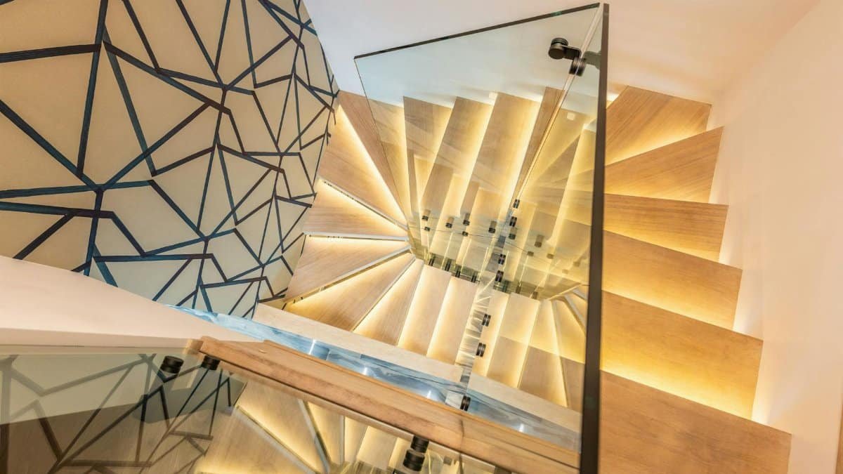 Modern interior featuring spiral wooden staircase with glass railing and artistic wall pattern.