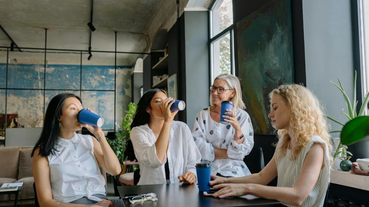 Group of diverse women sharing a coffee break in a modern office setting, fostering teamwork and collaboration.