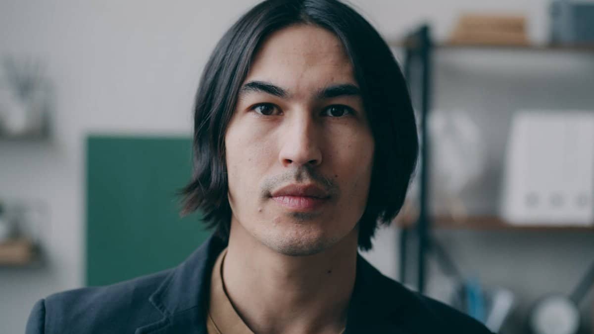 Portrait of a thoughtful adult man with long hair in an indoor setting.