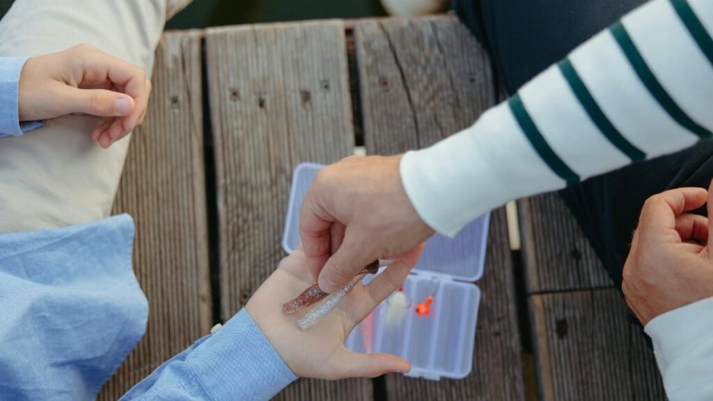 Parent and child selecting fishing lures from a tackle box on a wooden dock.