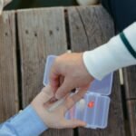 Parent and child selecting fishing lures from a tackle box on a wooden dock.