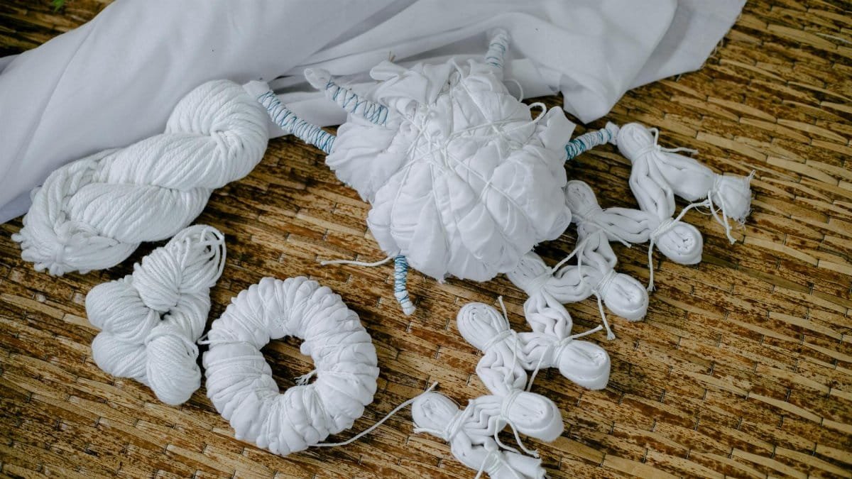 White textiles arranged for traditional Shibori dyeing technique on a woven mat.