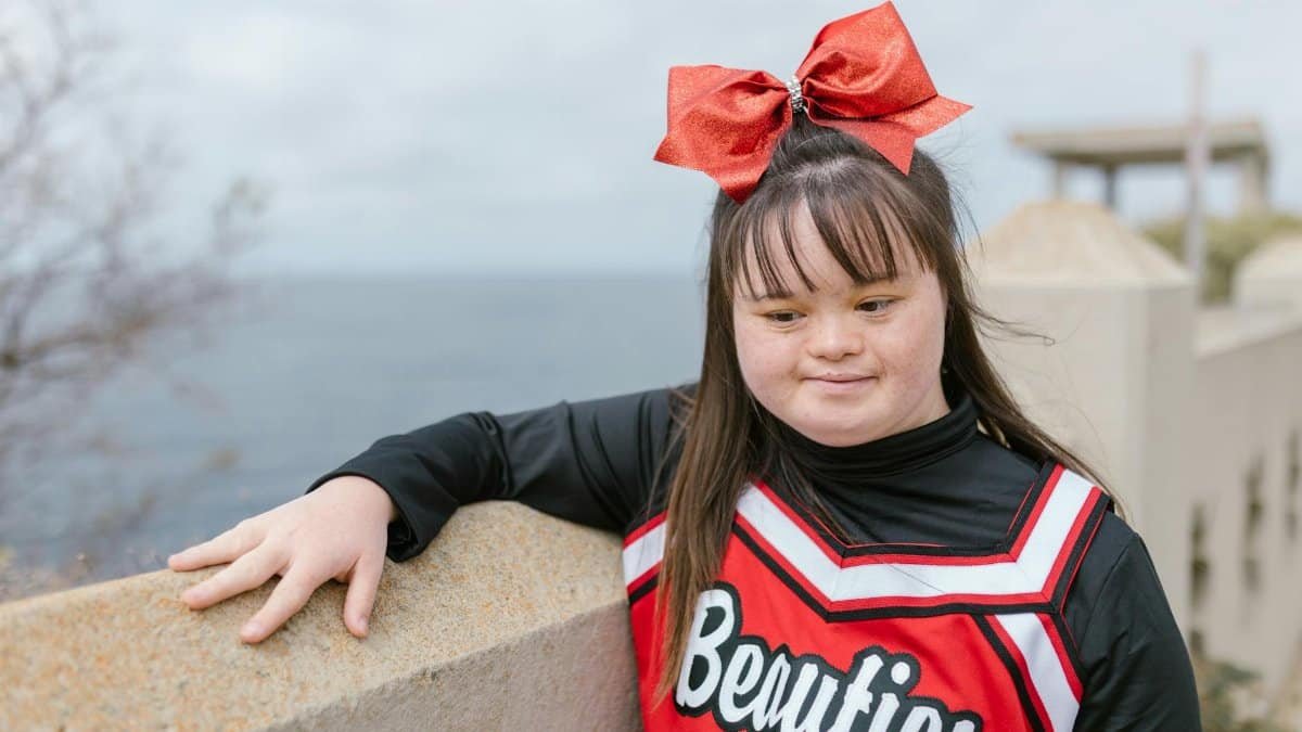 A young cheerleader with Down Syndrome poses confidently outdoors by the ocean.