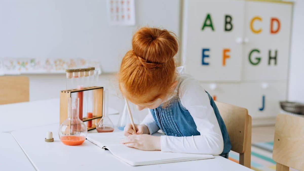 A young girl writing in a notebook, surrounded by test tubes, learning about science in a classroom.