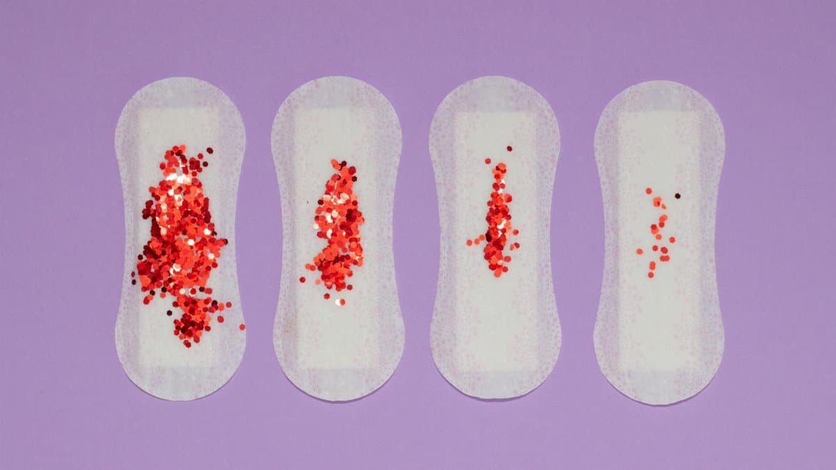 Four menstrual pads with red glitter, symbolizing menstruation, on a purple surface.