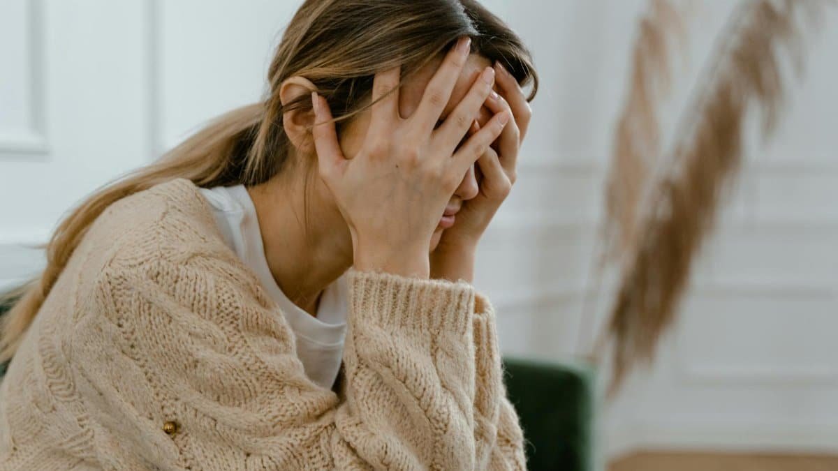 A woman sitting indoors covering her face in frustration, depicting stress and mental health challenges.