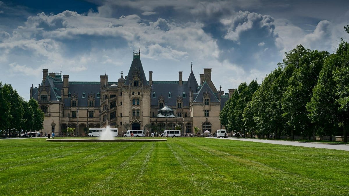 Stunning view of Biltmore Estate in Asheville with vibrant gardens and clear sky, showcasing architectural grandeur.