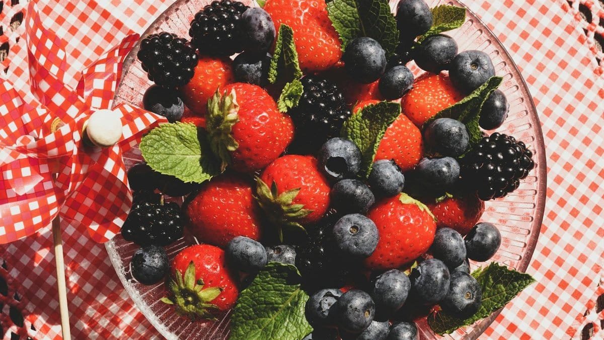 A vibrant mix of strawberries, blackberries, and blueberries with mint leaves in a glass bowl.