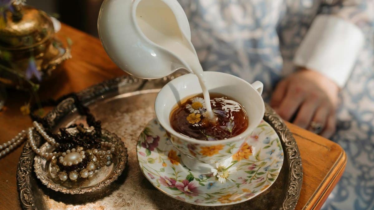 A vintage tea scene with milk being poured into chamomile tea, surrounded by pearls and ornate jewelry.