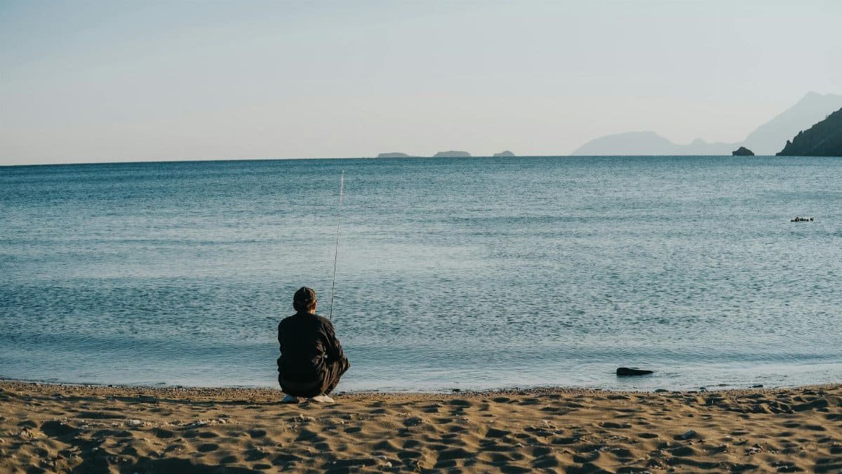 A solitary figure sits by the seaside fishing at dawn, exuding calm and tranquility.