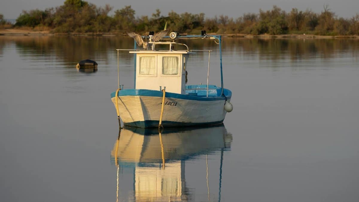 Calm fishing boat reflection on a quiet lake in Porto Cesareo, Italy.