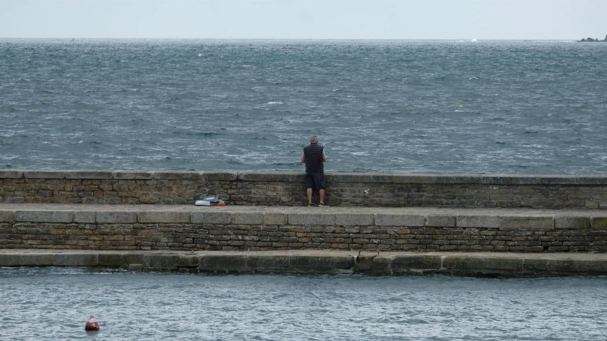 A lone person standing on a stone pier overlooking the ocean, capturing a moment of solitude and contemplation.